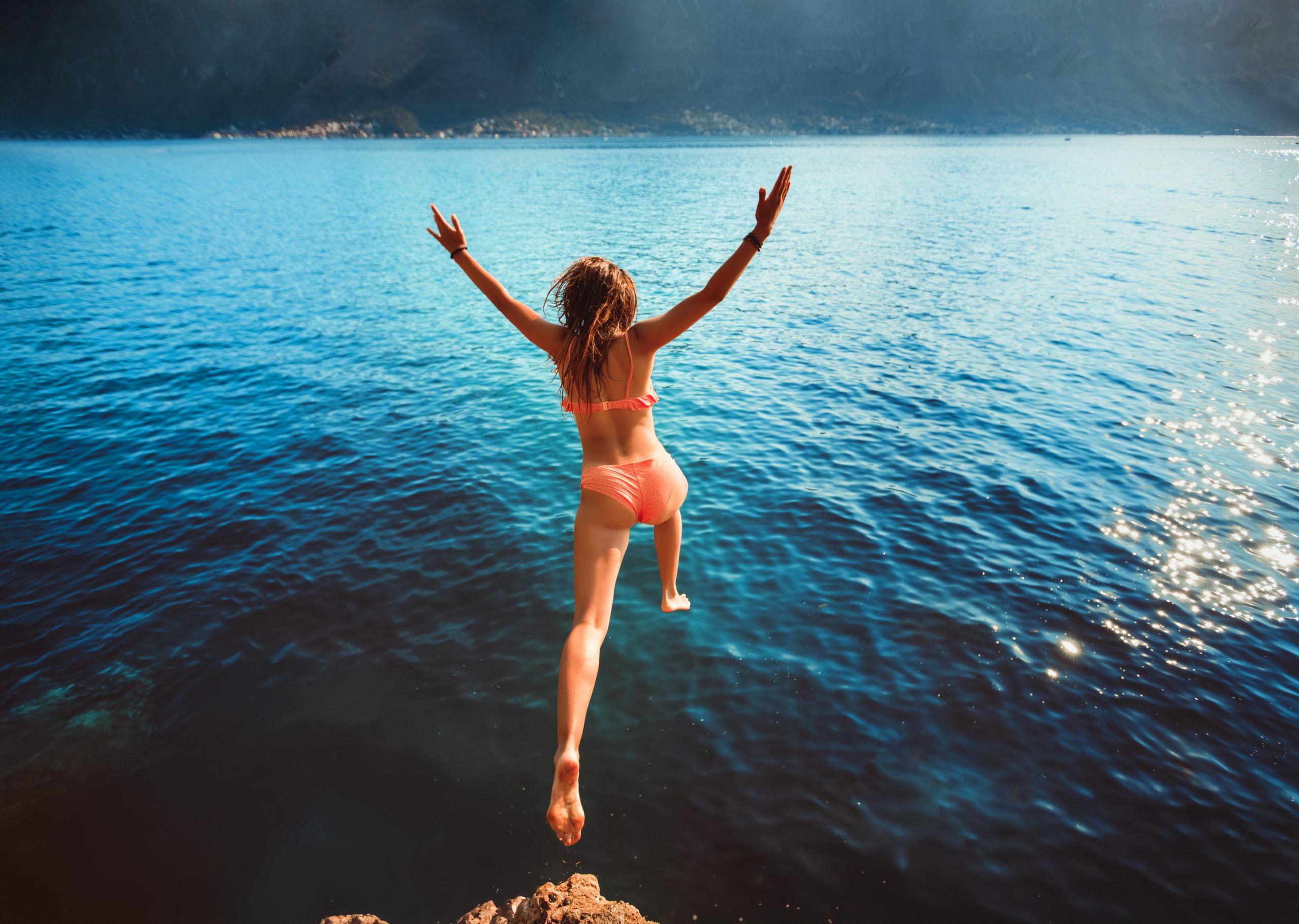 Healthy woman in bikini jumping off a rock into a lake.