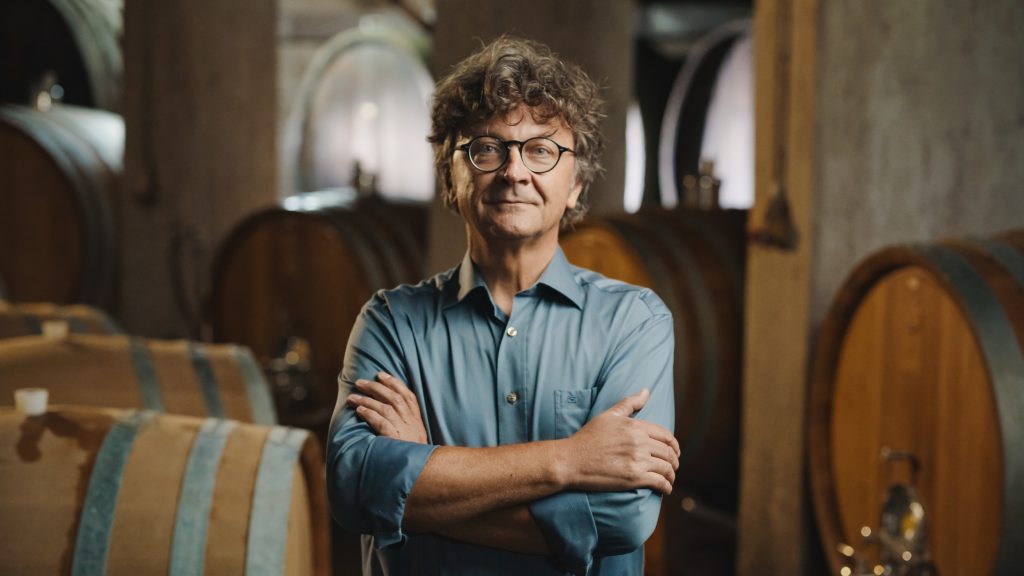 Defiant winemaker standing in front of barrels.