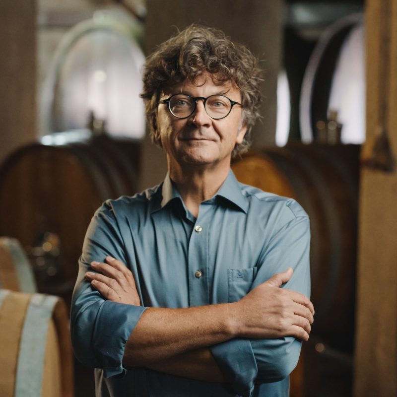 Defiant winemaker standing in front of barrels.